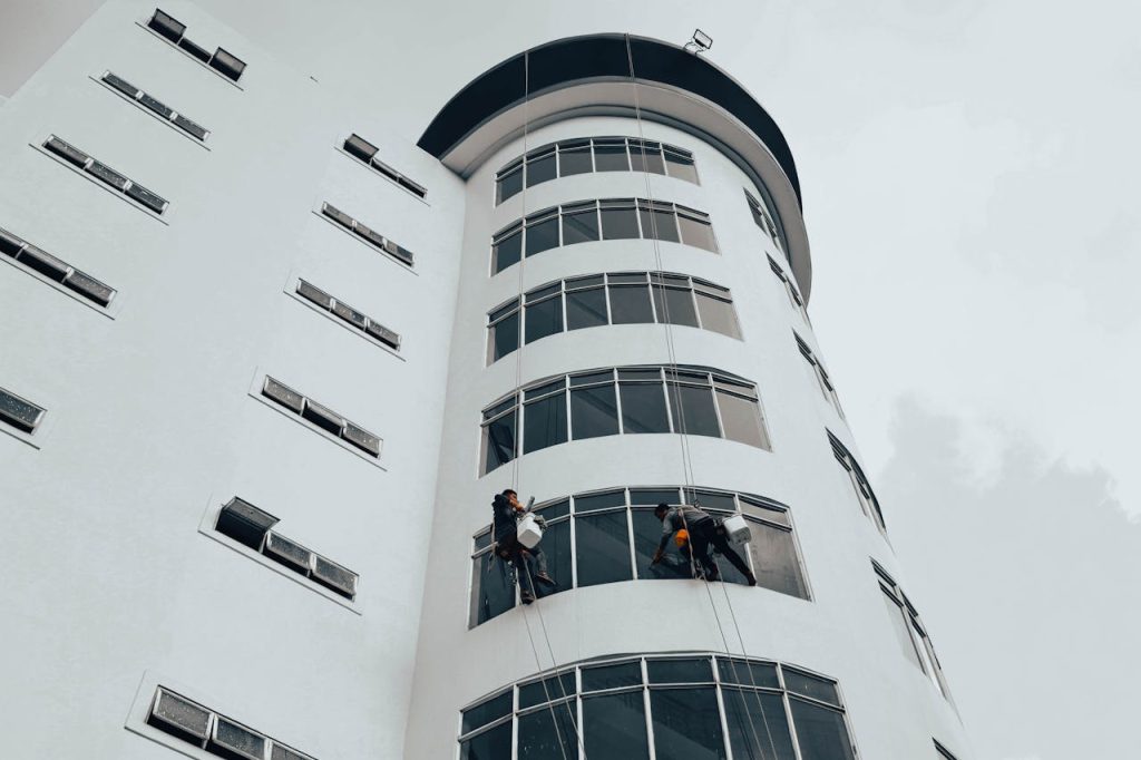 industrial-window-cleaning-on-modern-building-34517609 Workers cleaning windows on a modern high-rise building using ropes. Urban architectural maintenance.